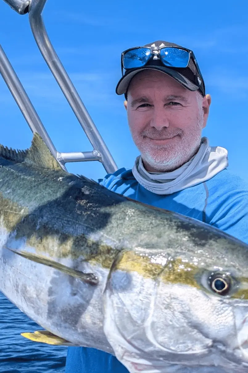Paul Bailey holding a large kingfish on a boat with a clear blue sky background